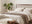 Mediterranean style bedroom with wood frame bed and neutral linens, light wood bedside table and bench at foot of bed