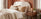 how to pick a bed buying guide banner - cosy bedroom with cream boucle fabric bed with soft orange and cream bedding, wooden bedside table, terracotta wall
