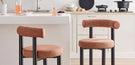tips for choosing the perfect bar stool - image features 2 modern styling bar chairs with teracotta orange fabric, barrel style round back cushion, round seta, and black round legs in modern kitchen