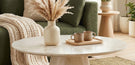 is a coffee table essential for living room design - features round cream marble pedestal coffee table in warm cosy living room with green sofa