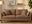 cosy living room with 3 seat brown faux leather sofa and angled floor lamp with round lampshade. Pot plans and wall art, and jute rug