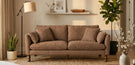 cosy living room with 3 seat brown faux leather sofa and angled floor lamp with round lampshade. Pot plans and wall art, and jute rug