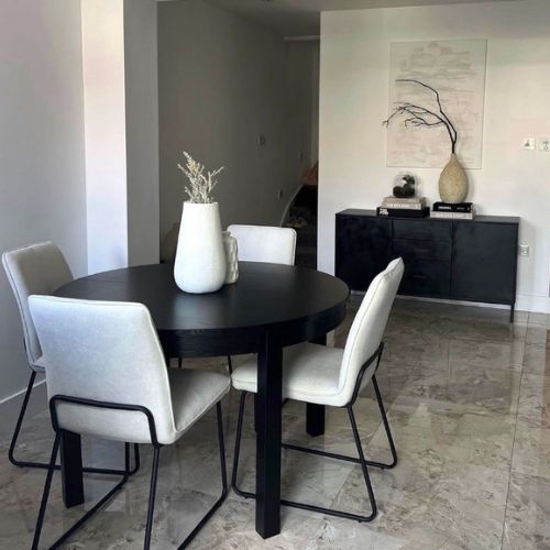 white and black dining space with round black dining table and 4 fabric dining chairs with trapezoid black metal legs