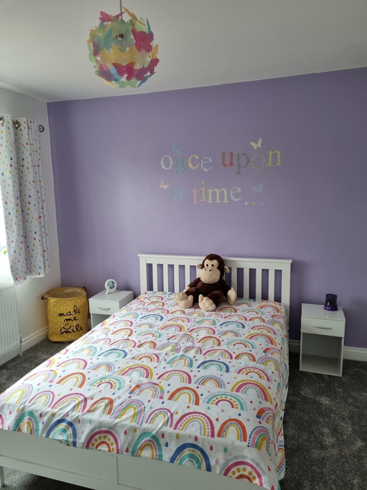 white solid pine bed in kid's bedroom with purple wall, monkey stuffed toy and white bedside tables.