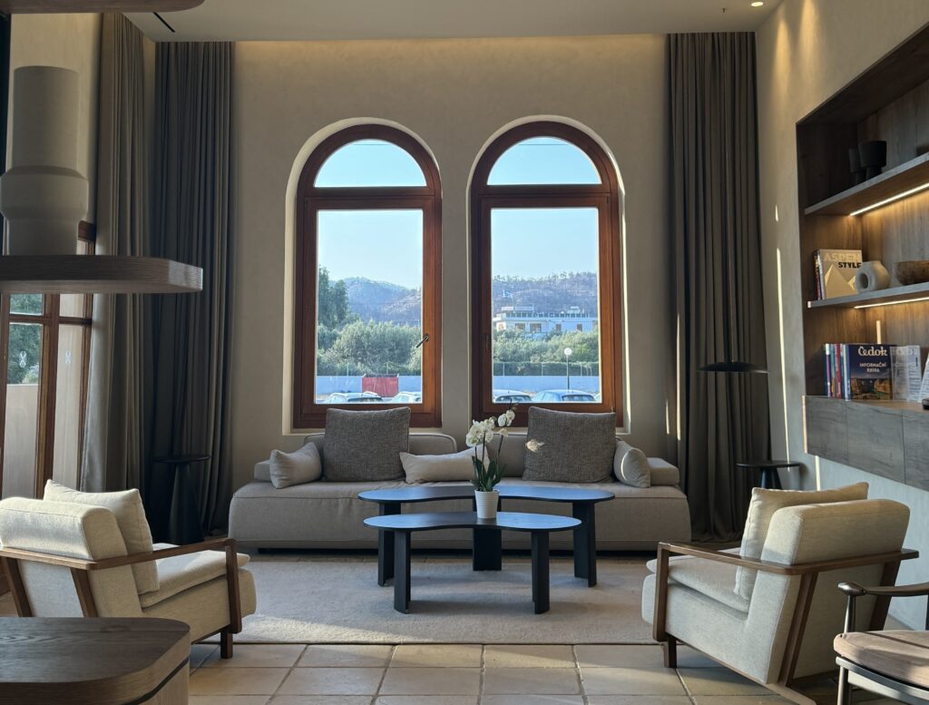 Lindian Village Beach Resort Rhodes shows quiet luxury interiors trend with minimalist decor in warm neutrals, with 2 arch windows overlooking the sea