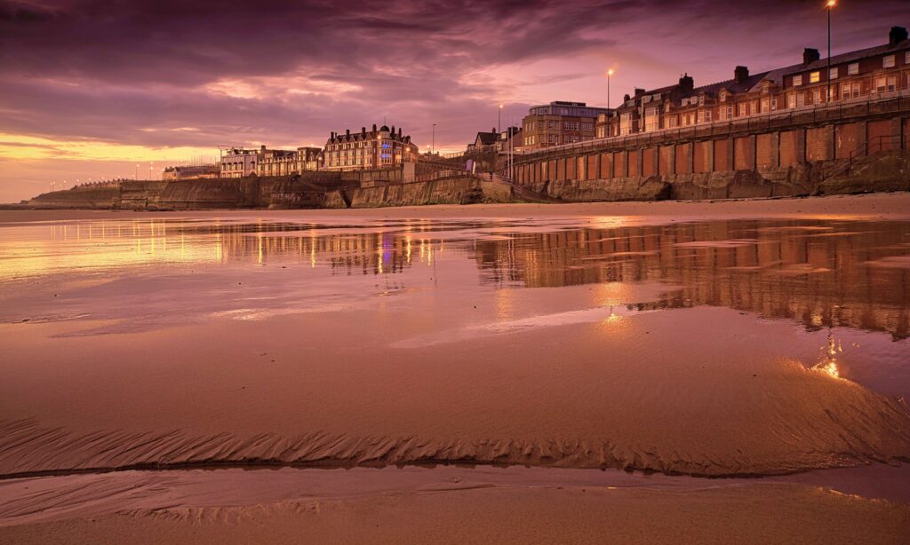 Whitley Bay beach at dusk with promenade and houses beyond. 