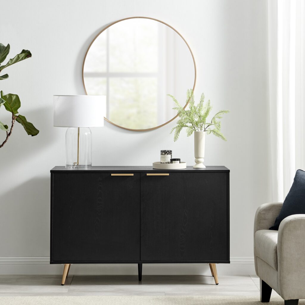 urban jungle furniture - black wood 2 door sideboard with copper coloured handles, with round wall mirror above, armchair to the right and potted plant to the left