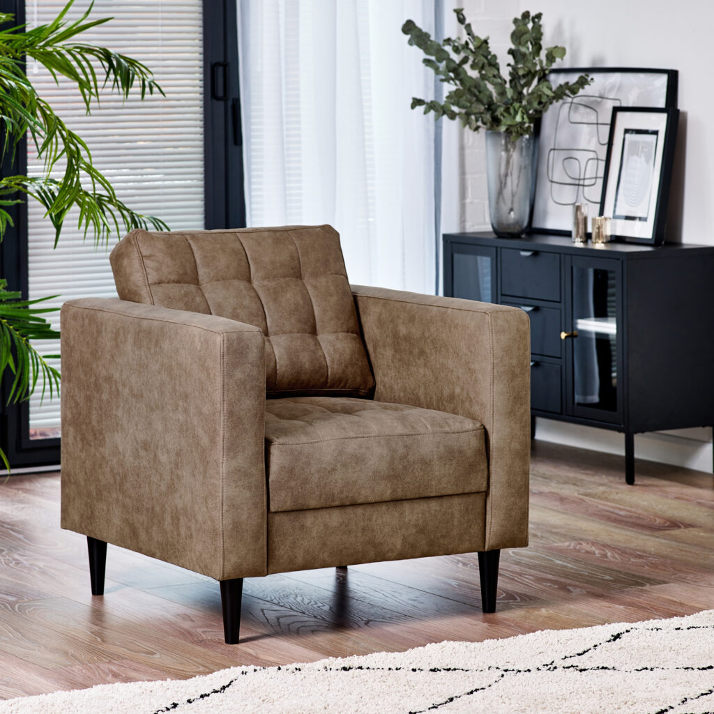 urban jungle furniture ideas - tan faux leather armchair with modern chesterfield style button tufting on back cushion, in modern living room with black metal sidebaord and potted plants