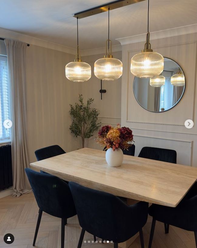 modern dining room with wooden and black metal dining table plus 6 black velvet chairs, and 3 glass pendant lights. Round wall mirror behind.