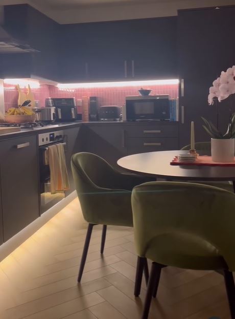 modern kitchen diner space with black cupbords, pink tiling, dark wood round dining tables and green dining chairs with orchid on table