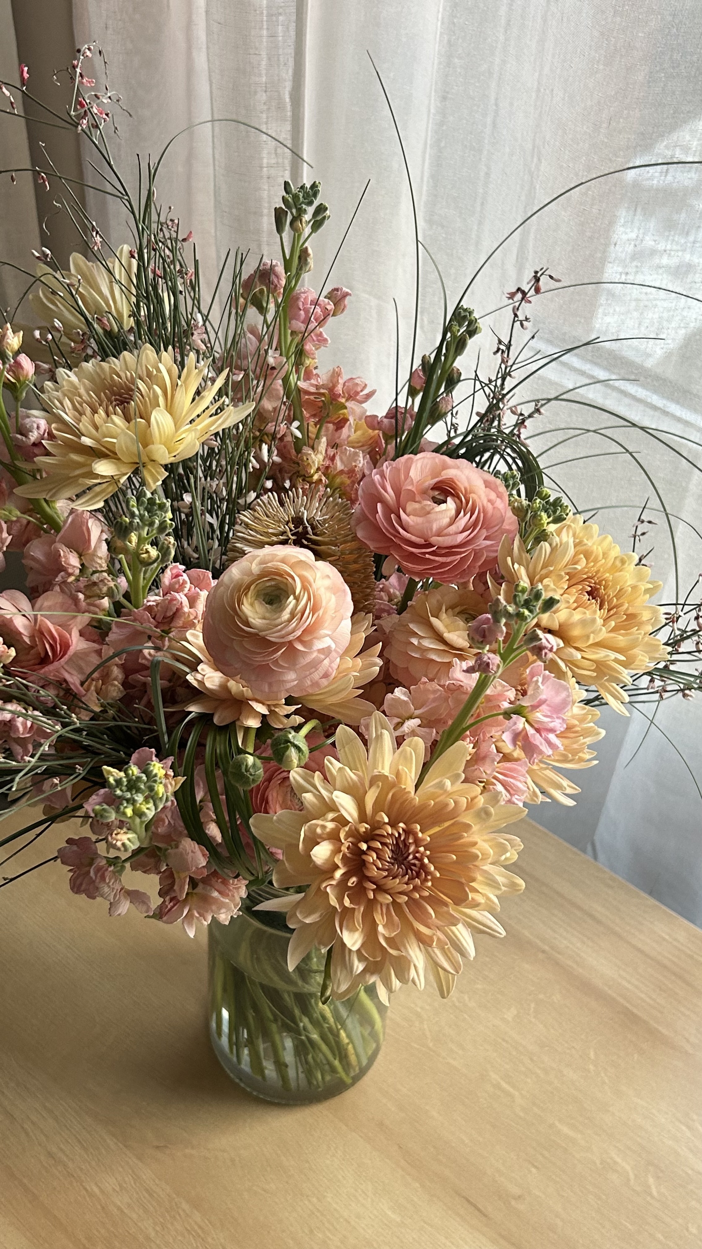 wooden desk in front of window with glass vase full of cottage style flowers